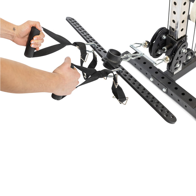 A person adjusts the Bells of Steel 30 D-Handle Bar Cable Attachment with Carabiners, featuring adjustable nylon handles, on a metal cable machine with pulleys and perforated beams against a white background.