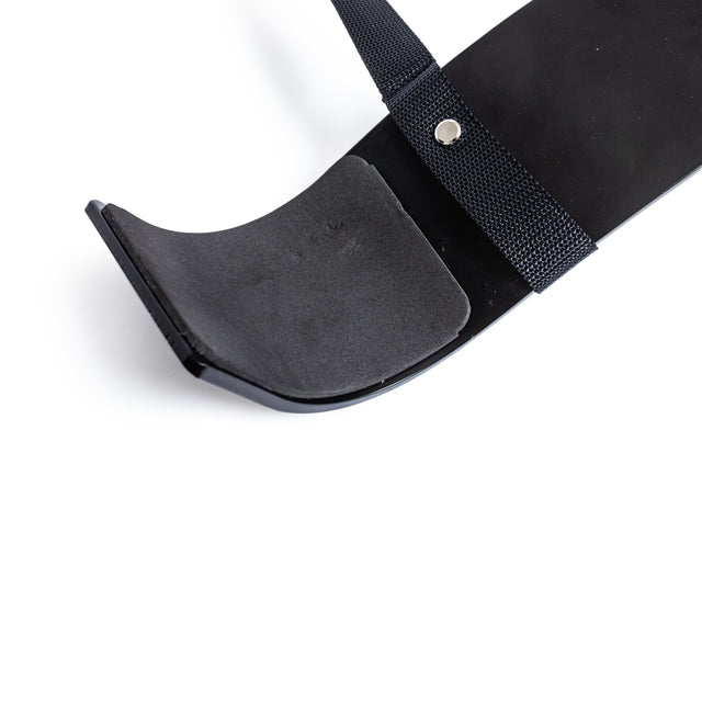 Close-up of the Bells of Steel Arm Blaster: a sturdy black plastic tool with a curved, padded end and strap secured by a metal rivet, resembling a curling tool, shown against a white background.