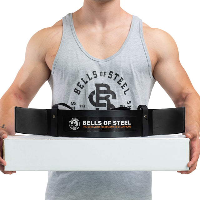 A person in a grey Bells of Steel tank top holds a white box with a black Bells of Steel Arm Blaster draped over it, ready for an intense biceps workout.