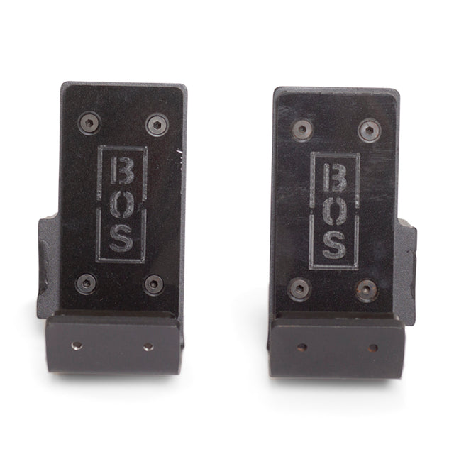 Two black Standard J-Cups by Bells of Steel, designed for power racks, feature "BOS" engraved vertically. Made of metal, they have visible screws, bottom mounting holes, and include UHMW protection to safeguard your equipment.