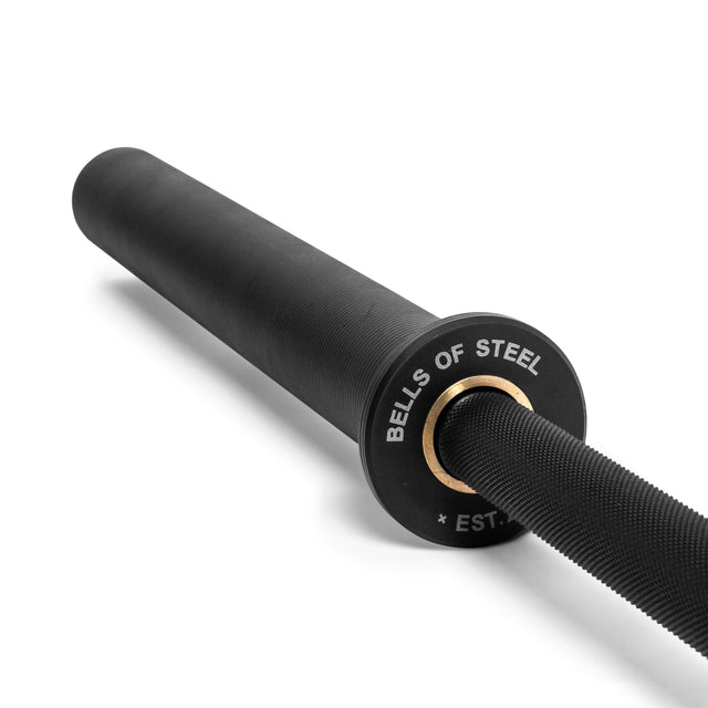 A close-up of the Bells of Steel Powerlifting Bar with "BELLS OF STEEL" and "EST." in white on the end cap, shown against a white background—an ideal budget-friendly power bar choice.