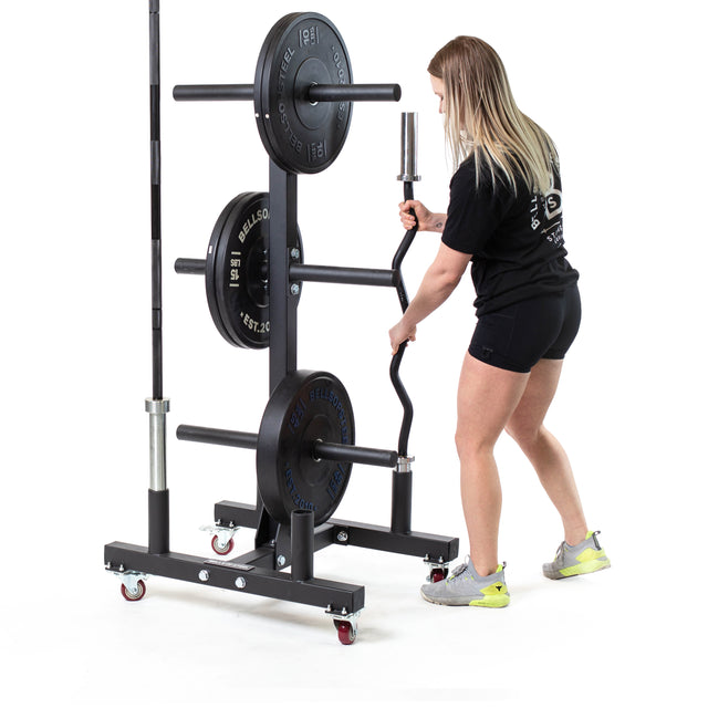Wearing athletic wear, a person places a hex bar onto the Bells of Steel Bumper Plate Weight Tree And Bar Holder, which stores plates and barbells on wheels for mobility; the background is white.