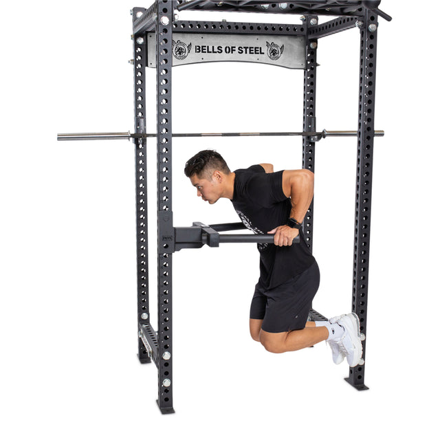 An athlete in workout gear performs tricep dips on a Y Dip Bar Rack Attachment within a Bells of Steel power rack, maintaining a strong and focused posture mid-motion.