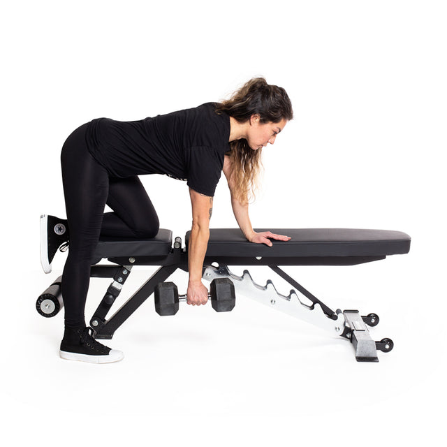A woman in black athletic wear uses a Bells of Steel Ergo Rubber Hex Dumbbell Set to perform a one-arm row, bracing herself on a workout bench, with a white background.
