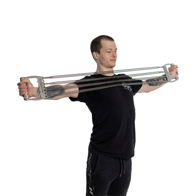 A person wearing black shirt and pants uses the Bells of Steel Chest Expander, equipped with multiple metal springs, to build lean muscle by stretching it outward with both arms extended.