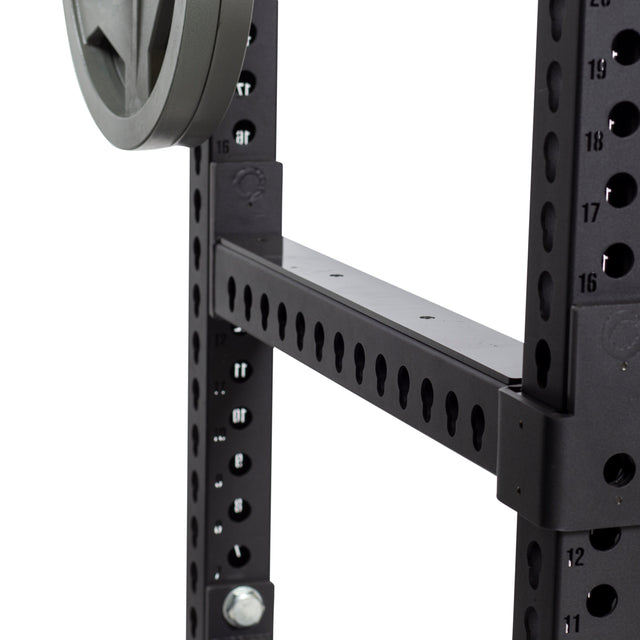 Close-up of the Bells of Steel Flip-Down Safeties on a black metal power rack with numbered holes, a horizontal support bar, and a weight plate on one side for added training safety.