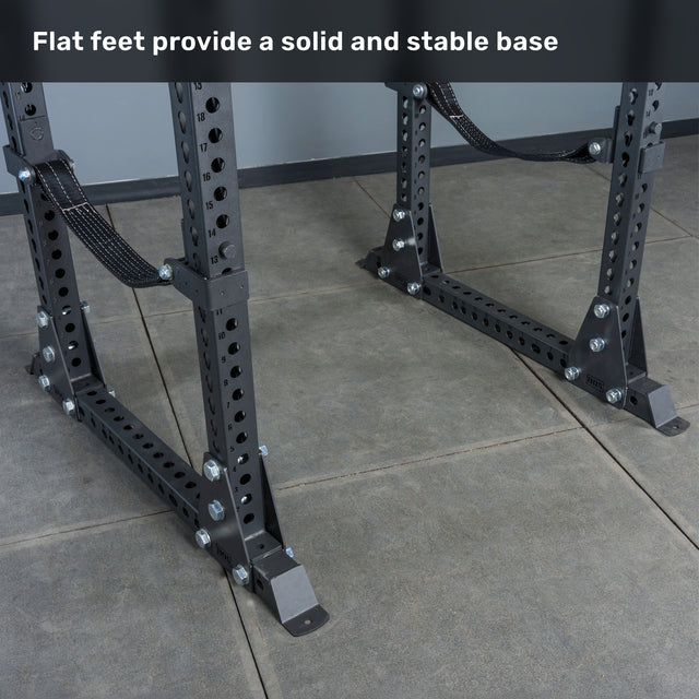 Two Bells of Steel Manticore Flat Foot Power Rack Builder bases (3" x 3", 1" holes) with multiple bolt holes and flat feet rest on a tiled floor. Perfect for a home gym setup, the text above reads, "Flat feet provide a solid and stable base.