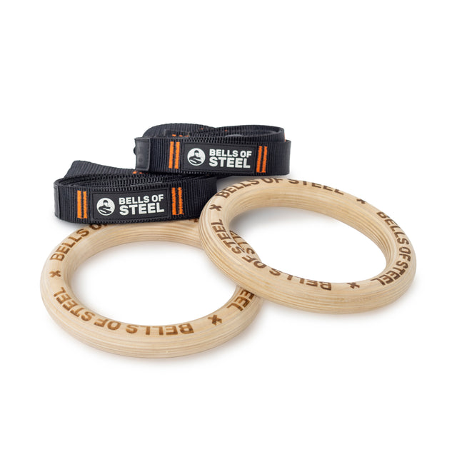 Bells of Steel Gymnastics Rings with black adjustable straps and orange details are perfect for bodyweight training, displayed on a white background. Ideal for enhancing your core workout routine.
