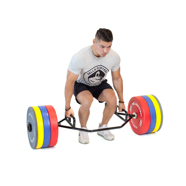 A man in a light gray t-shirt and black shorts prepares to lift the Bells of Steel Open Trap Bar / Hex Bar, loaded with colorful weight plates and rotating sleeves, set against a white background.