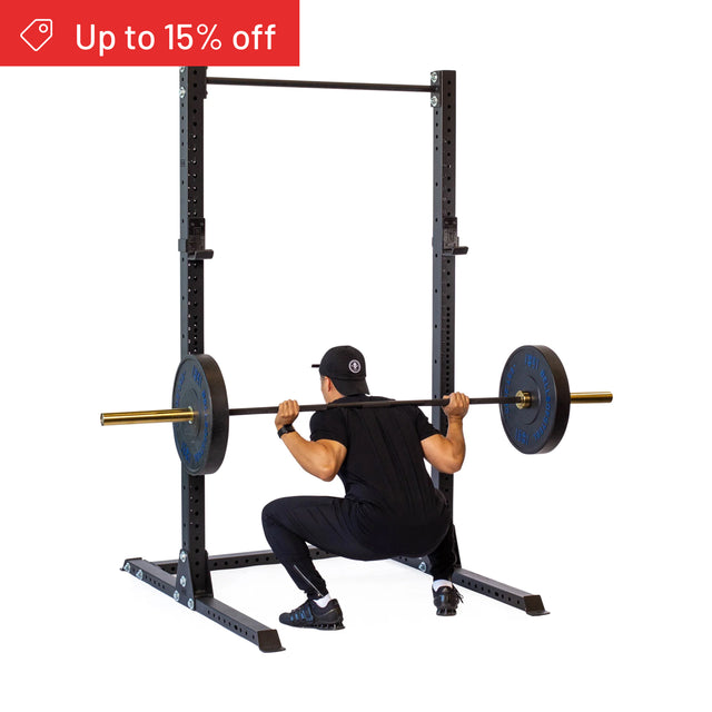 A person squats with a loaded barbell on their shoulders in a Bells of Steel Hydra Squat Stand Builder (3" x 3", ⅝" Holes), an ideal fit for home gyms. A red "Up to 15% off" label appears in the top left corner.