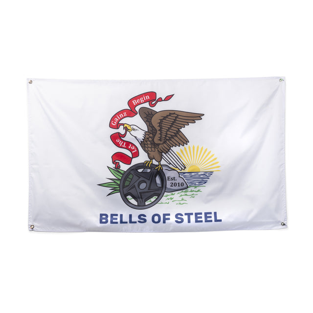 Bells of Steel Flags: Gym decor featuring an eagle with a "Let Gains Begin" ribbon, standing on a barbell plate by water and grass, with "Est. 2010"—a perfect addition to your home gym setup.