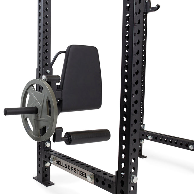 A Bells of Steel Leg Curl / Leg Extension Rack Attachment with a padded backrest and rotating weight plate holder is mounted on a steel power rack.