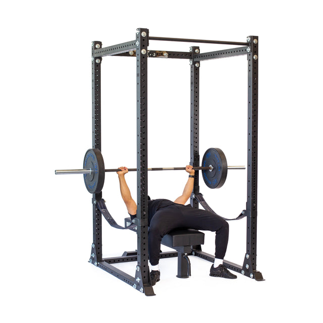 A person bench presses on a bench inside the Bells of Steel Hydra Flat Foot Power Rack Builder (3" x 3", ⅝" Holes), arms extended and feet flat—an ideal addition to any home gym.