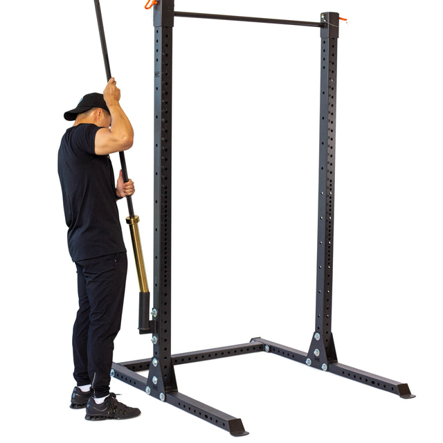 A person in black uses the Bells of Steel Vertical Mount Barbell Holder Rack Attachment on a power rack, efficiently organizing barbells in a home or gym setting.