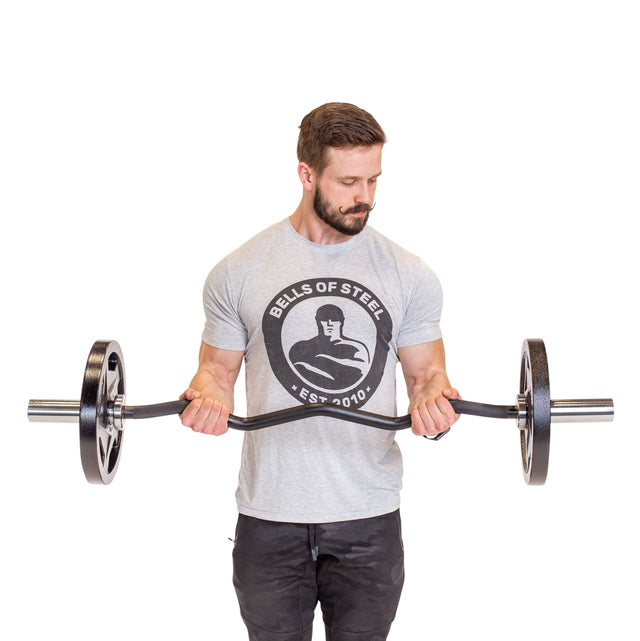 A bearded man in a gray Bells of Steel t-shirt and black pants stands against a white background, holding the Bells of Steel EZ Curl Bar (45") loaded at waist height, looking down at the bar.
