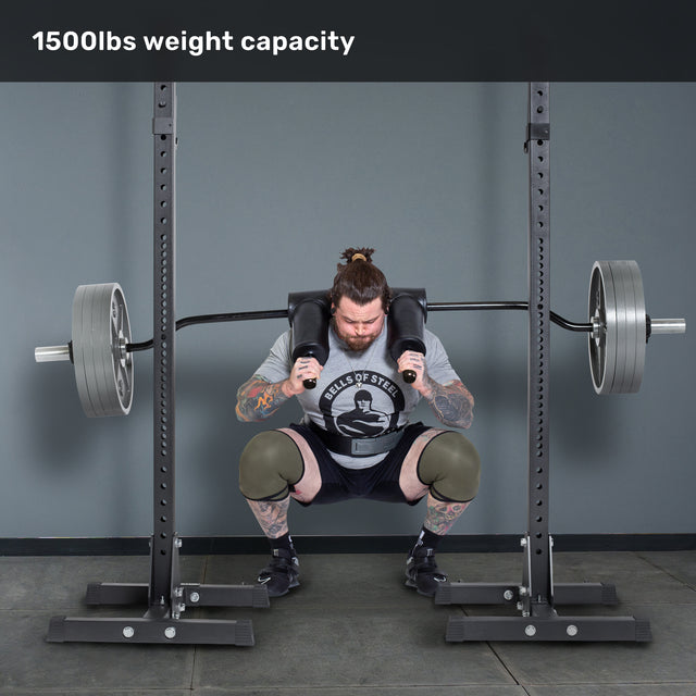 A man with tattoos and knee sleeves squats a loaded Bells of Steel Safety Squat Bar - The SS4 on a rack. Text above says "1500lbs weight capacity." Perfect gear for your next leg day.