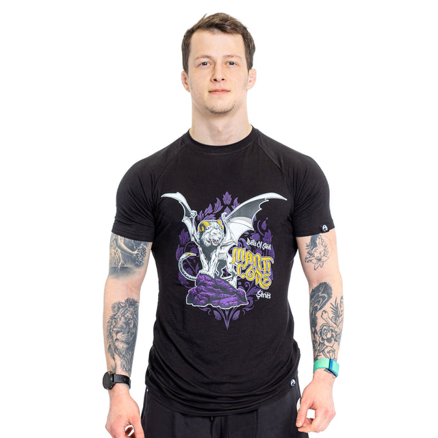 A tattooed man wears a Bells of Steel Bamboo T-Shirt with a white lion, bat wings, purple accents, and stylized text, standing against a white background.