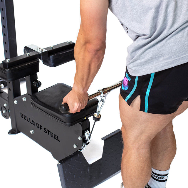 Dressed in shorts and a T-shirt, someone grips the handle of a Bells of Steel Lat Pulldown Low Row Machine, ready for cable exercises with this versatile home gym equipment.