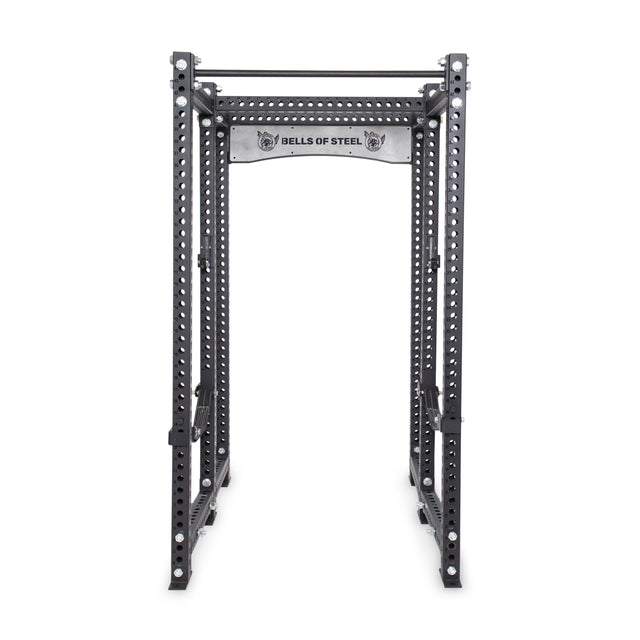 The Manticore Six Post Power Rack - Prebuilt by Bells of Steel is a sturdy black structure with 1" adjustment holes and a pull-up bar. Its modular components offer versatile setups, and the brand name is prominently displayed on the metal support beam.