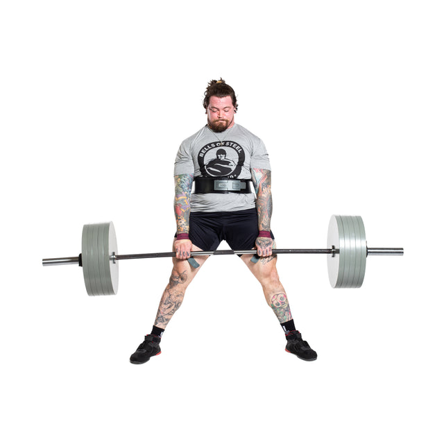 A tattooed man in a gray t-shirt and black shorts performs a sumo deadlift with the Bells of Steel Powerlifting Bar, which meets IPF specs, showing determination against a plain white background.