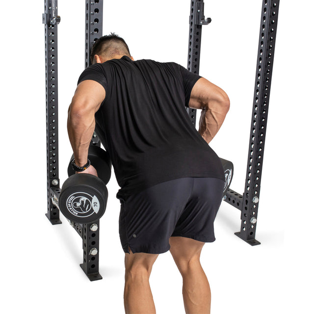 A man uses the Bells of Steel Seal Row Pad Rack Attachment to perform a bent-over dumbbell row inside a power rack, lifting two dumbbells.