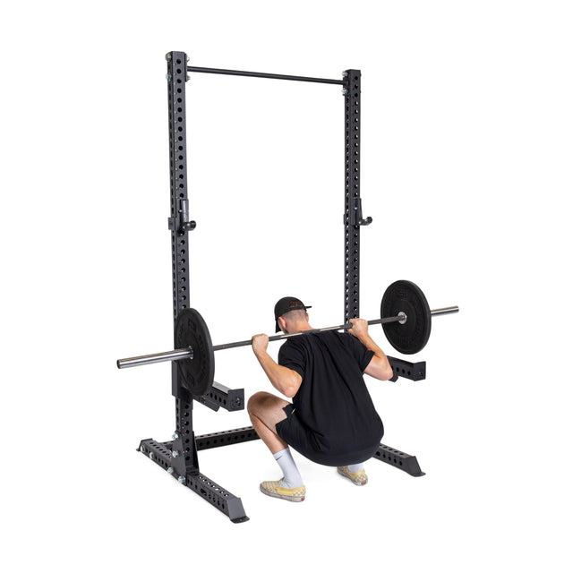 A person in black athletic gear squats with a barbell inside the Bells of Steel Manticore Squat Stand Builder (3"x3", 1" holes), creating a pro-level home gym vibe against a white background.