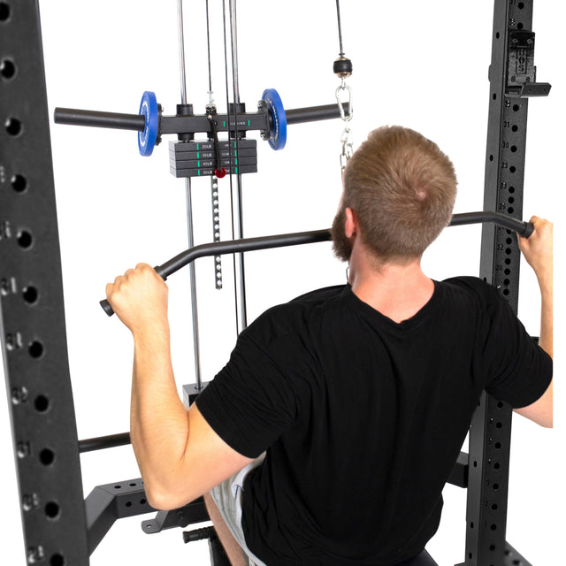 A man grips the Bells of Steel Lat Pulldown & Low Row Rack Attachment (Hydra & Manticore), seated on a workout bench, preparing for cable exercises with visible equipment, weights, and the low row attachment.