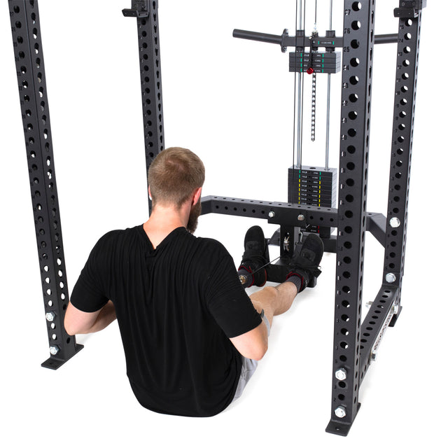 A man sits on the floor of a Bells of Steel Hydra & Manticore Lat Pulldown & Low Row Rack Attachment, preparing to perform a seated cable row with a straight bar.