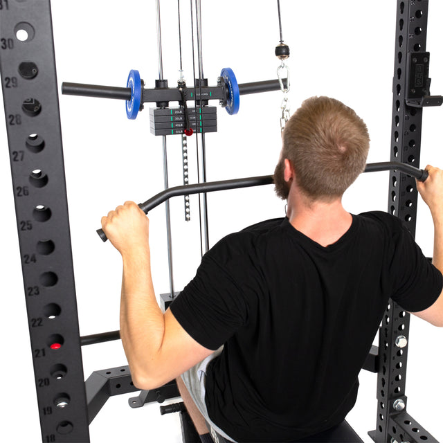 A man uses the Bells of Steel Lat Pulldown & Low Row Rack Attachment – Hydra & Manticore in a gym, gripping the bar overhead while seated, with Olympic plates and cable system visible against a white background.