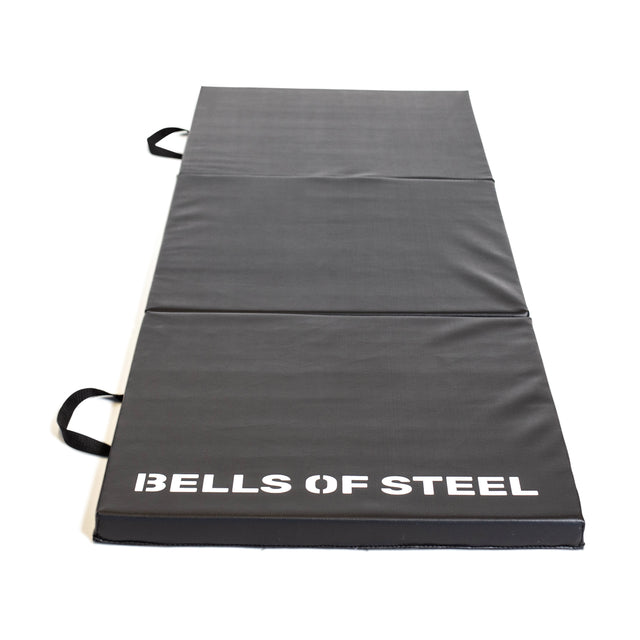 The Bells of Steel Trifold Mat is a black, non-slip exercise mat with side handles and "BELLS OF STEEL" in white text—perfect for gymnastics or workouts.