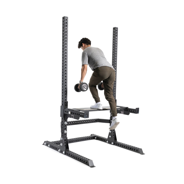 A person in athletic clothes does a step-up exercise with a dumbbell on the Bells of Steel Utility Seat for Hydra/Manticore, featuring adjustable platforms, against a white background.