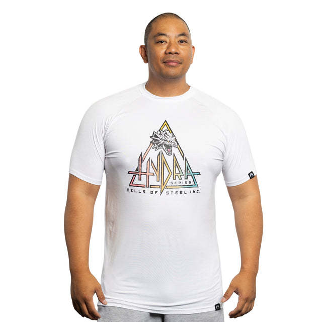 A man faces forward against a plain white background, wearing a white Bamboo T-Shirt from Bells of Steel featuring a colorful geometric Hydra design and the text "HYDRA SERIES BELLS OF STEEL INC.