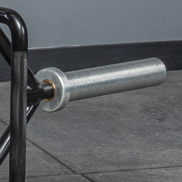 Close-up of the Bells of Steel Open Trap Bar's end resting on a gray tiled gym floor, highlighting its smooth silver rotating sleeves and sturdy black frame.