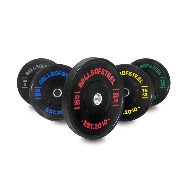Five vibrant Dead Bounce Conflict Bumper Plate Sets by Bells of Steel—10 kg (white), 15 kg (yellow), 20 kg (blue), 25 kg (red), and 5 kg (green)—are upright, displaying durable virgin rubber and a dead bounce for safety.