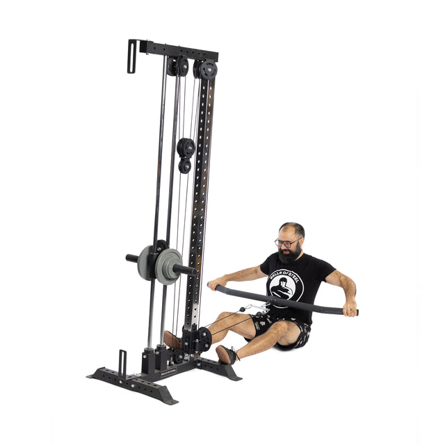 A bearded man with glasses uses the Bells of Steel Fat Bar - Lat Pulldown Bar on a seated row machine, sitting on the floor with legs extended, to test his grip strength against a white background.