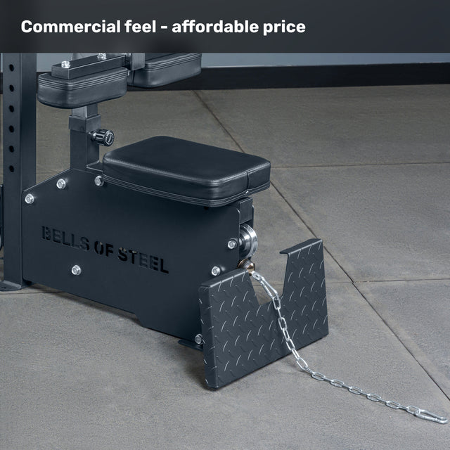 A close-up of the Bells of Steel Lat Pulldown Low Row Machine with padded seat, metal platform, and chain on a concrete gym floor. Text at the top reads: "Commercial feel - affordable price.