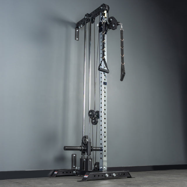 The Bells of Steel Cable Tower stands against a gray wall on a tiled gym floor, featuring a visible weight stack and multiple attachment handles, ready for diverse cable machine exercises.