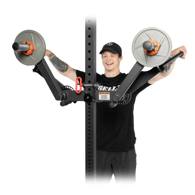 A man in a black shirt and cap demonstrates the Bells of Steel Shoulder Boulder/Chest Fly Attachment, showing its capability for targeted shoulder or arm exercises with weighted plates on a vertical rack.