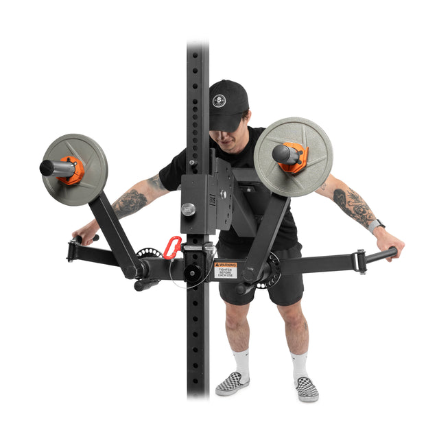 Wearing a black hat, black clothes, checkered shoes, and showing tattoos on both arms, a person uses the Bells of Steel Shoulder Boulder/Chest Fly Attachment power rack add-on to perform shoulder and chest isolations.