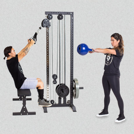 A person seated using a cable machine for a pull exercise, and another person performing a kettlebell swing. Both are wearing black workout attire. The background is plain gray.