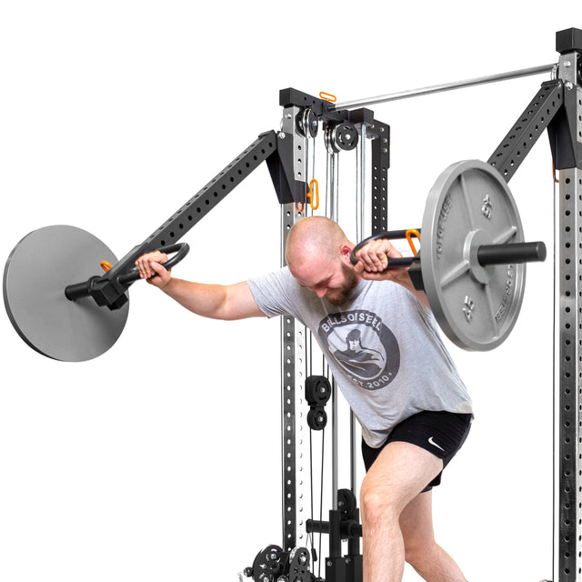 A man in athletic wear does a landmine press on Bells of Steel Cable Tower Squat Stands, pressing a loaded barbell overhead from a lunging stance.