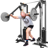 A man in a gray t-shirt and black shorts performs an angled barbell press on the Bells of Steel Cable Tower Squat Stands, using two cable arms with weight plates, in a gym.