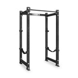 The Bells of Steel Manticore Four Post Power Rack - Prebuilt features sturdy 3" x 3" uprights with 1" holes for adjustable attachments, reinforcing bars, and safety straps. Designed for weightlifting and strength training in your home gym, this black steel power rack stands out against a white background.