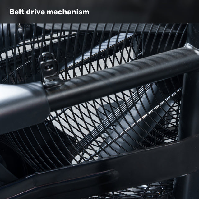 Close-up of the belt drive on the Bells of Steel Residential Air Bike with Wind Guard, showing metal blades behind a wire mesh and a sturdy bar in front. Caption: "Belt drive mechanism"—ideal for any home gym.