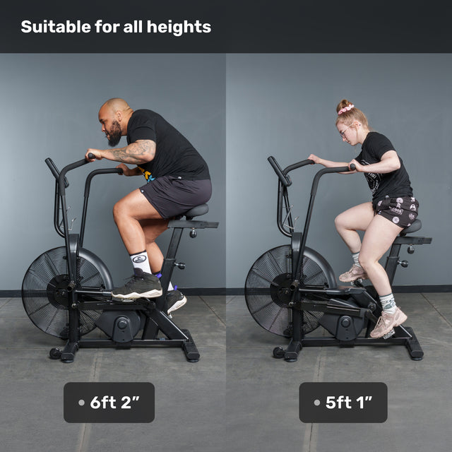 Two people—one 6'2" and one 5'1"—ride the Bells of Steel Residential Air Bike with Wind Guard together, proving it suits users of any height. Text above reads, "Suitable for all heights." Perfect addition to any home gym.