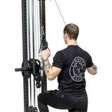 A tattooed person in a black "Strength Equipment" shirt uses Bells of Steel Adjustable Length Aluminum Handles on a cable machine for a lat pulldown, kneeling with a white background that highlights these premium gym accessories.