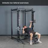 Wearing a black shirt and shorts, a person performs a bench press in the gym using Bells of Steel Anvil Handles. The unilateral handles allow each arm to be isolated for a balanced, iso-lateral workout. Above, the text reads: “Unlocks iso-lateral exercises.”.