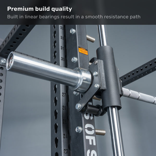 Close-up of a Smith machine barbell and track system, highlighting the solid metal construction and built-in linear bearings for smooth resistance. Anvil Handles by Bells of Steel, or other iso-lateral attachments, can be added for versatile unilateral training options. Text overlay reads “Premium build quality” and “Built-in linear bearings result in a smooth resistance path.”.