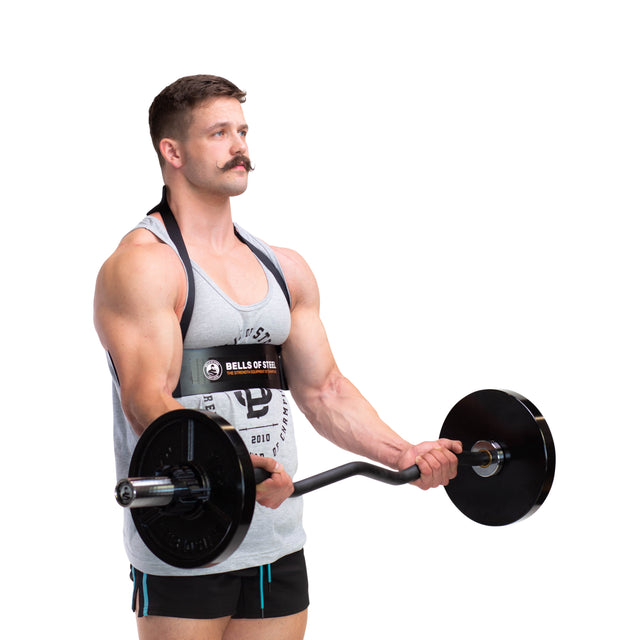 A muscular man in a tank top and shorts performs bicep curls with a barbell, using the Bells of Steel Arm Blaster for support. The background is plain white.