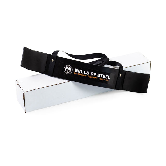 A Bells of Steel Arm Blaster sits atop a plain white box. Ideal for supporting heavy lifts in intense biceps workouts, it features the brand's logo and the tagline “The Strength Equipment of Champions.”.